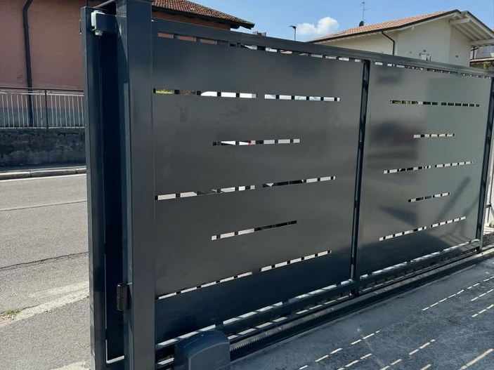 Cancello scorrevole grigio antracite con fessure orizzontali, motore e cremagliera alla base, in una via residenziale